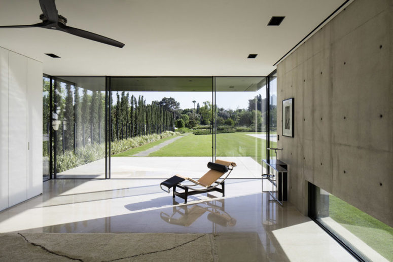 One of the walls is glass, with doors, which lead to the garden, and tall trees act as a living fence