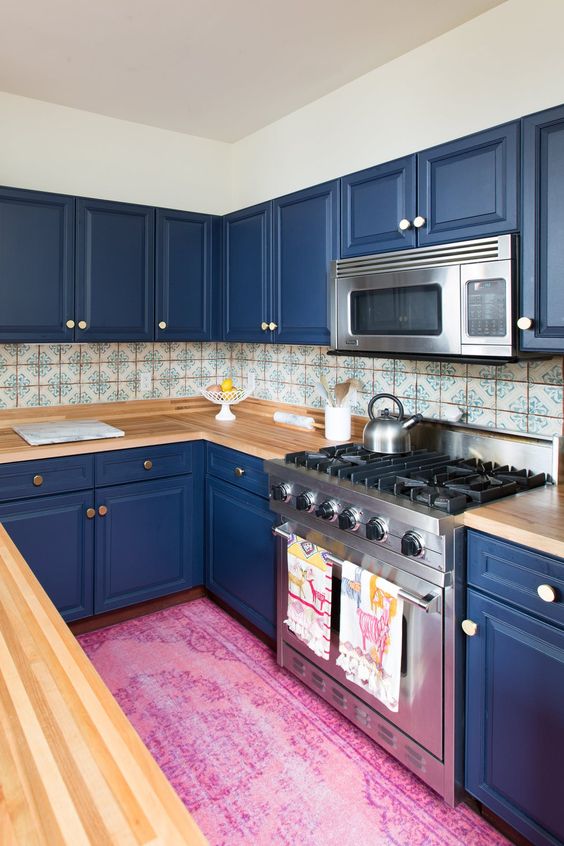 a bold blue kitchen with light-colored wooden countertops and a mosaic tile backsplash