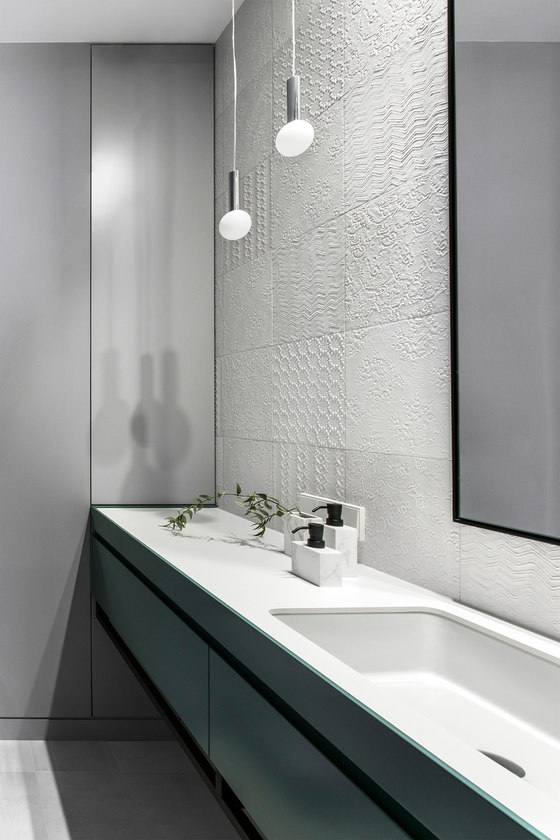 The bathroom was decorated with white tiles of different textures, a green vanity and a mirror