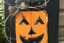 16 a black pallet sign with a bold orange Jack-o-lantern, a ribbon bow