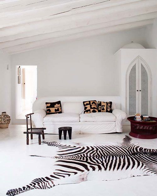 a large zebra print rug and dark stools accentuate a white living room