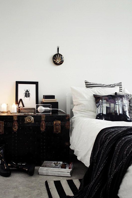a vintage black trunk with copper detailing serves as a nightstand and a storage piece and it looks amazing