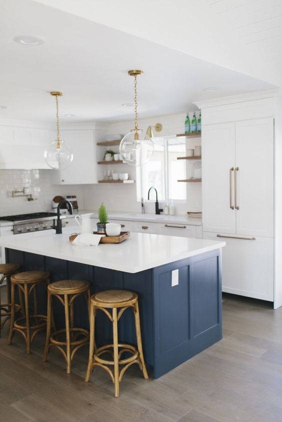 a chic vintage kitchen with brass touches and a dark blue island and wooden stools