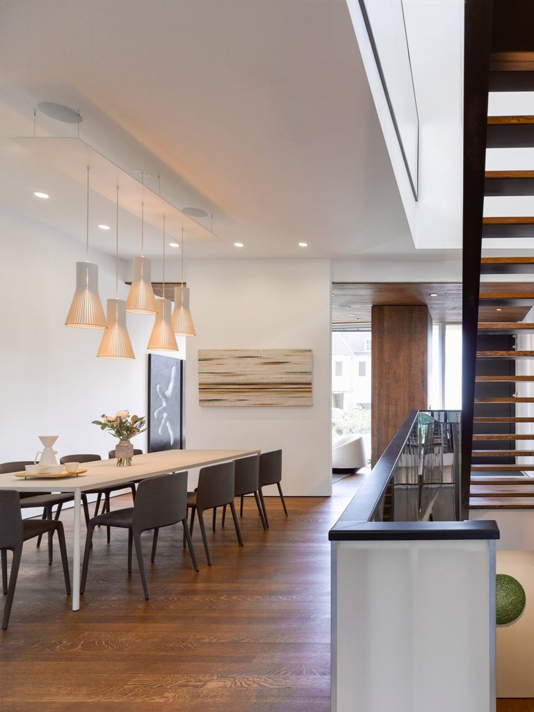 The dining area is done with cool lamps, black modern chairs and a light-colored dining table