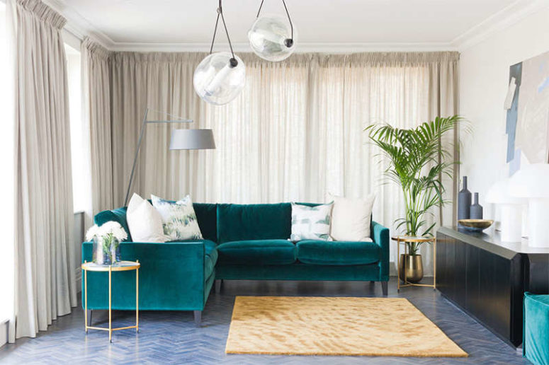 The calm and peaceful kitchen is made more eye-catchy with a living space and a bold emerald velvet sofa and a black sideboard