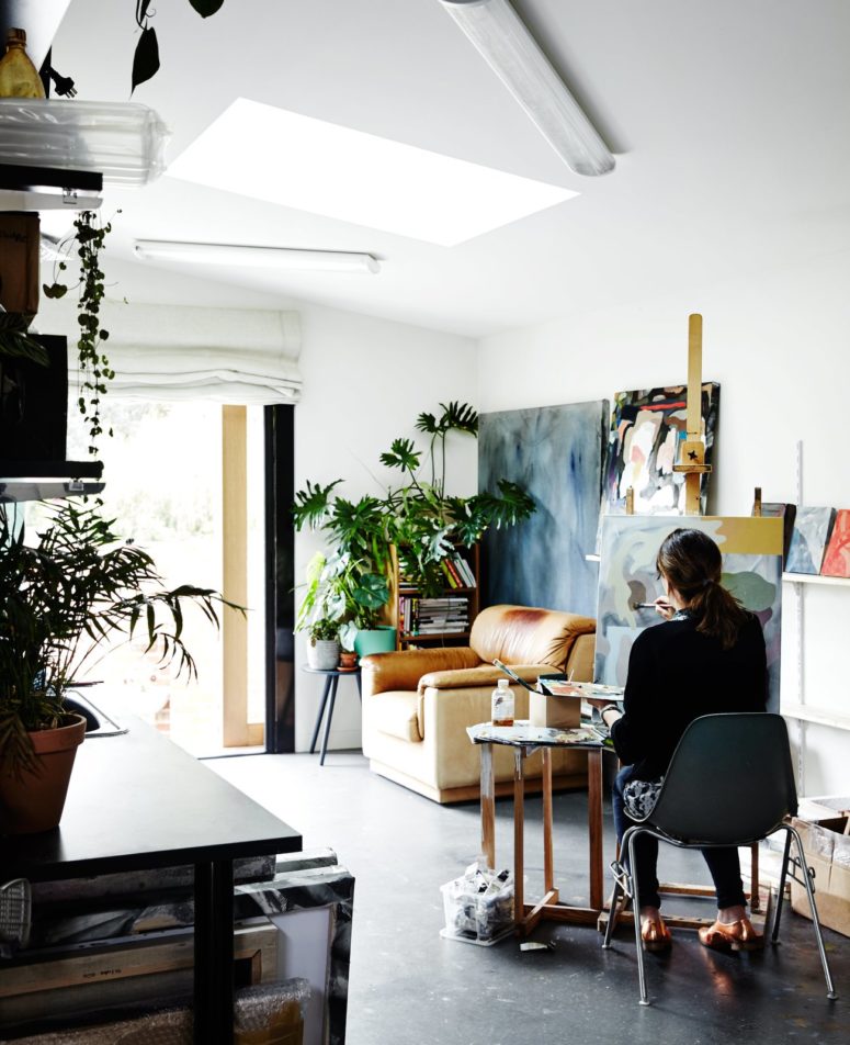 The living room and studio in one is done with a lot of greenery, cozy furniture and there's a comfy nook for painting here