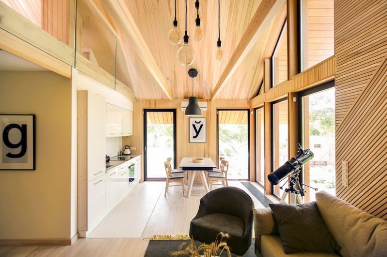 There's a light-colored kitchen with a dining zone and lots of large windows that bring light and nature inside