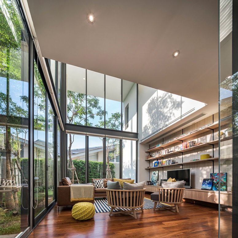 The living room features extensive glazing, a large shelving unit, a sitting space that seems to be outdoors due to the strong connection with it
