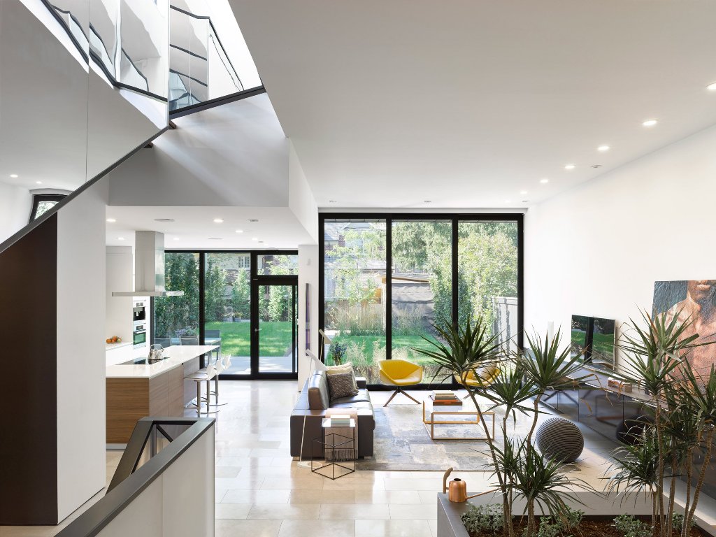 The living room is united with the kitchen and features a glazed wall, greenery and simple modern furniture