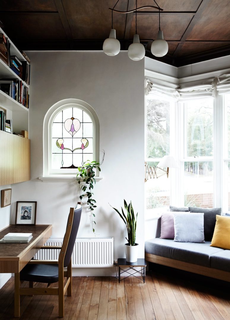 This is a small home office with a cool shape, a mosaic window, a comfy desk and a storage unit over it, and a sofa is placed into the niche