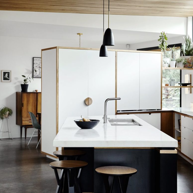 The kitchen is done with cool white cabinets with wooden handles, a large kitchen island with a white countertop, which doubles as a breakfast zone