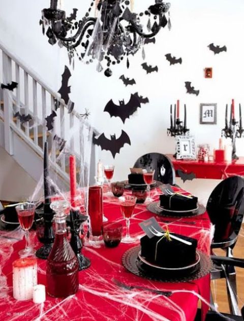 a bold black and red tablescape with red candles, a red tablecloth, bats around and a black chandelier with spider webs