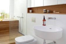 06 a white space with a wooden built-in shelf, a wood clad shower and bathtub and sleek white panels