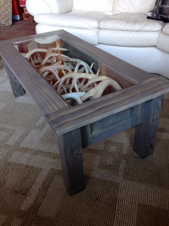 a coffee table of reclaimed wood with antlers inside and a glass tabletop to enjoy looking at them