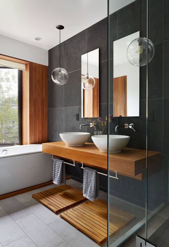 a modern bathroom with black and grey tiles, saturated wood mats and a vanity and a white tub