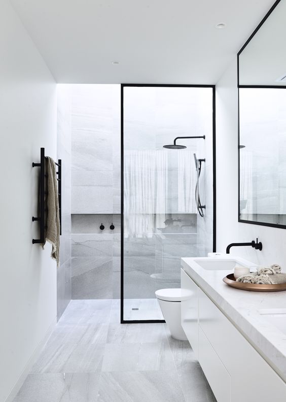 a modern space with grey marble tiles, white cabinets, black frame glass door and faucets