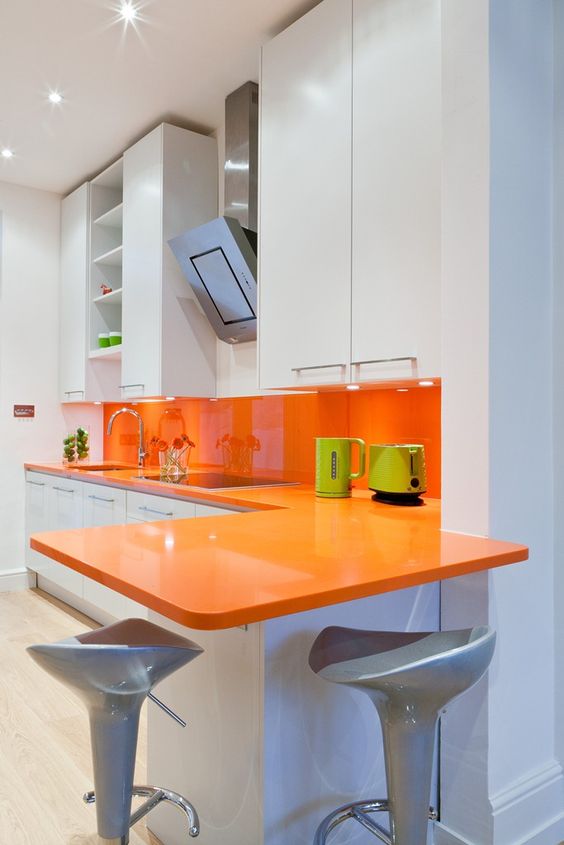 a minimalist white kitchen is made bolder with an orange backsplash and countertops