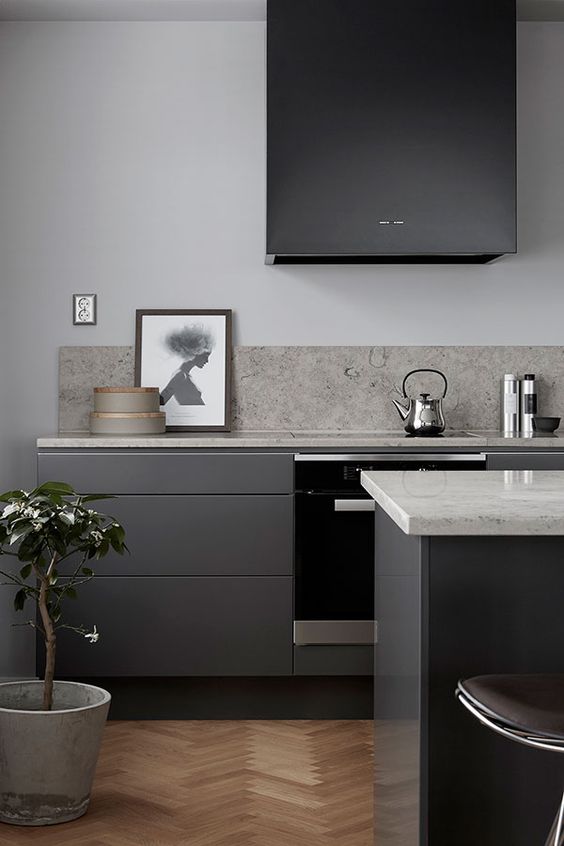 a modern sleek dark grey kitchen with a black hood, white countertops and a grey stone backsplash looks very stylish