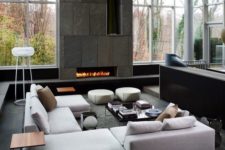25 a modern moody living room with double height ceilings, a stone fireplace wall and light grey upholstered furniture