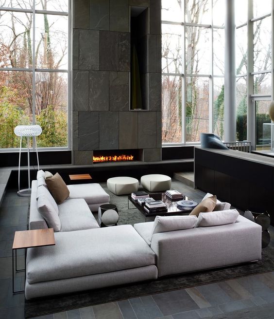 a modern moody living room with double height ceilings, a stone fireplace wall and light grey upholstered furniture