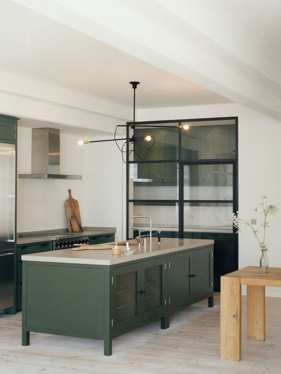 dark green cabinets and a kitchen island with modern lights and a glass pantry for a modenr space