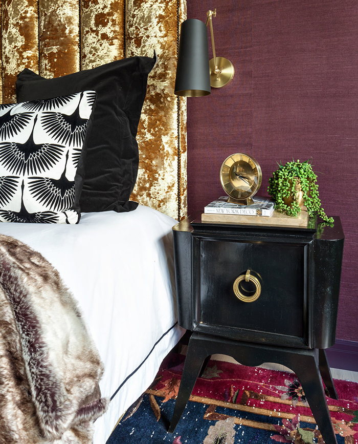 The bed is upholstered with crushed gold velvet, there are black nightstands and various brass touches