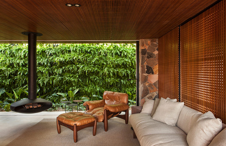 The living room features comfy contemporary furniture and a hanging fireplace, the space is opened to outdoors when necessary and there's a green wall