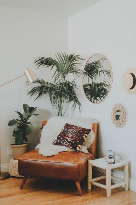 a boho nook with a leather chair, some potted greenery, a mirror and a lamp makes up a cozy reading space