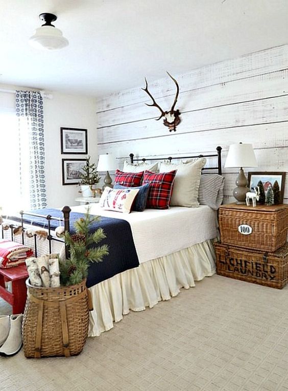 a cozy rustic bedroom dressed up for winter with a whitewashed wood wall, a basket with evergreens and pinecones, antlers