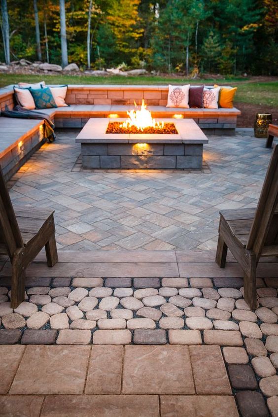 a patio clad with stone and stone benches with a wooden top for cozy sitting by the fire