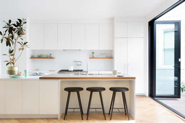 The cabinets are sleek, with no handles, there's a white backsplash and some open shelving
