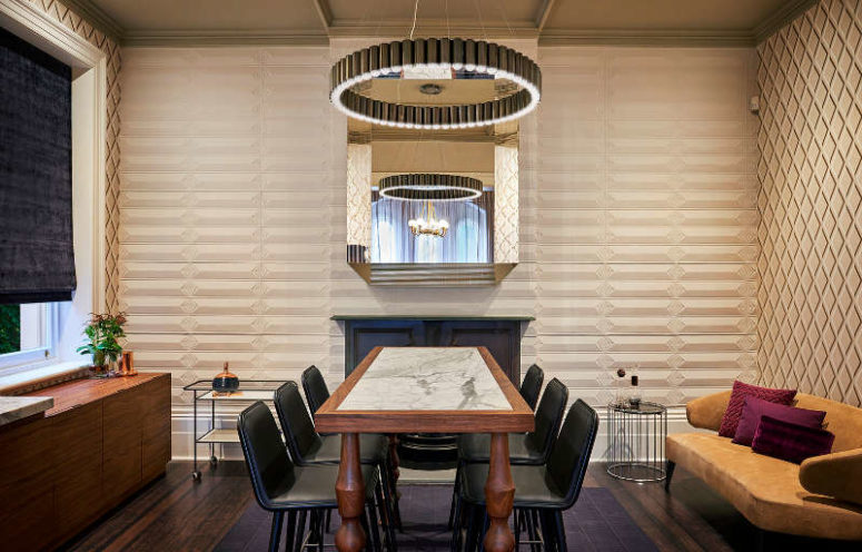 The dining room is centered around a whimsy table with a marble inlay, a metallic chandelier and a large glam mirror