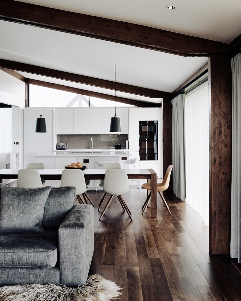 The kitchen is done in white, there are wooden beams and floors, and a dining set with a wooden table and white chairs