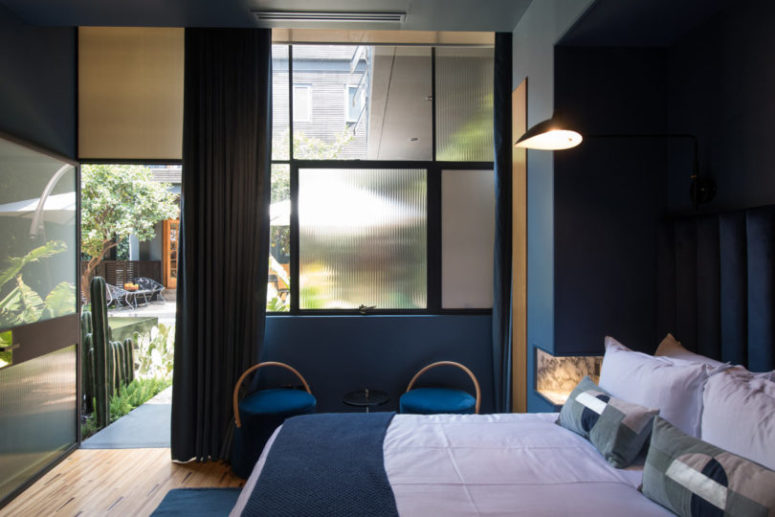 This s ablue guest room with velvet chairs, a comfy bed and a glazed wall