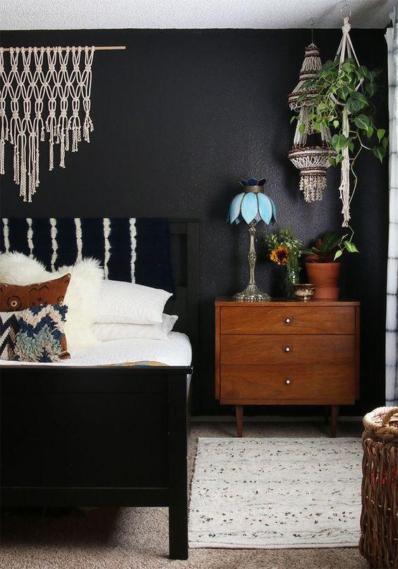 a boho chic bedroom with a black wall, lots of macrame and texture looks very warm and welcoming