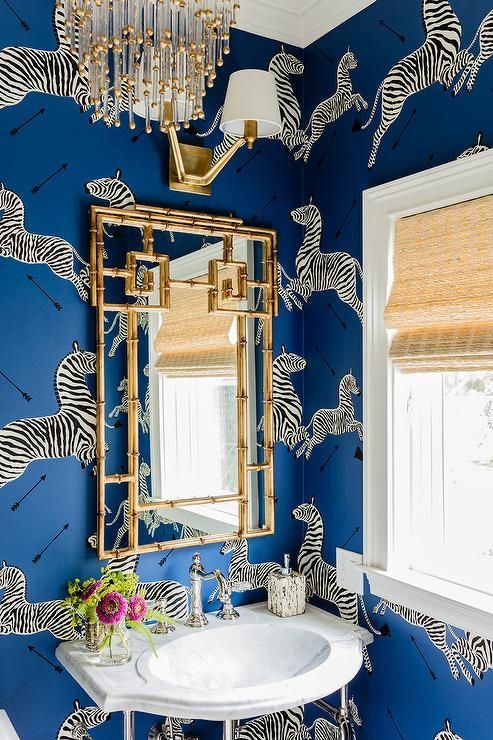 bold blue wallpaper with a zebra print and a gilded frame mirror mka eup the whole look of this space