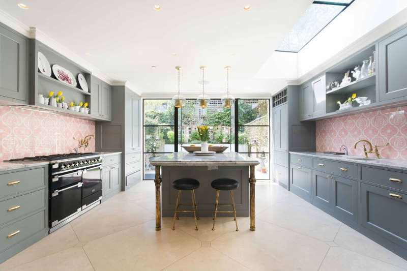The kitchen is done in graphite grey, with pink patterned tile backsplashes and some brass touches