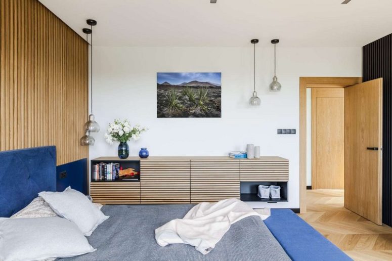 The master bedroom features a wooden slat wall and a floating sideboard and a blue upholstered bed