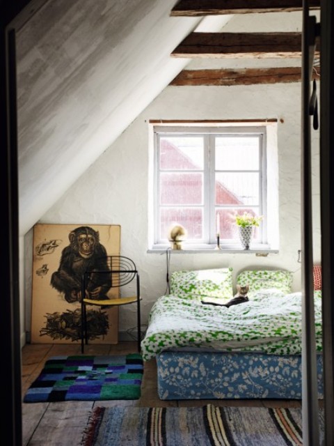 A guest bedroom is an attic space with wooden beams, colorful boho textiles and floral printed bedding for a cool boho feel