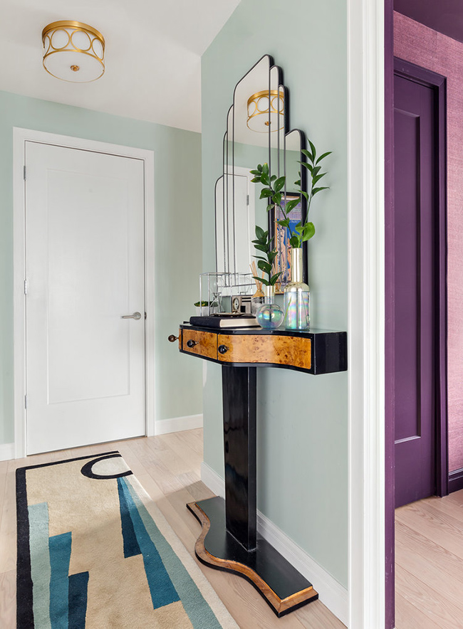 The entryway features a bold art deco console table and mirror of a very eye-catchy shape and a geo rug