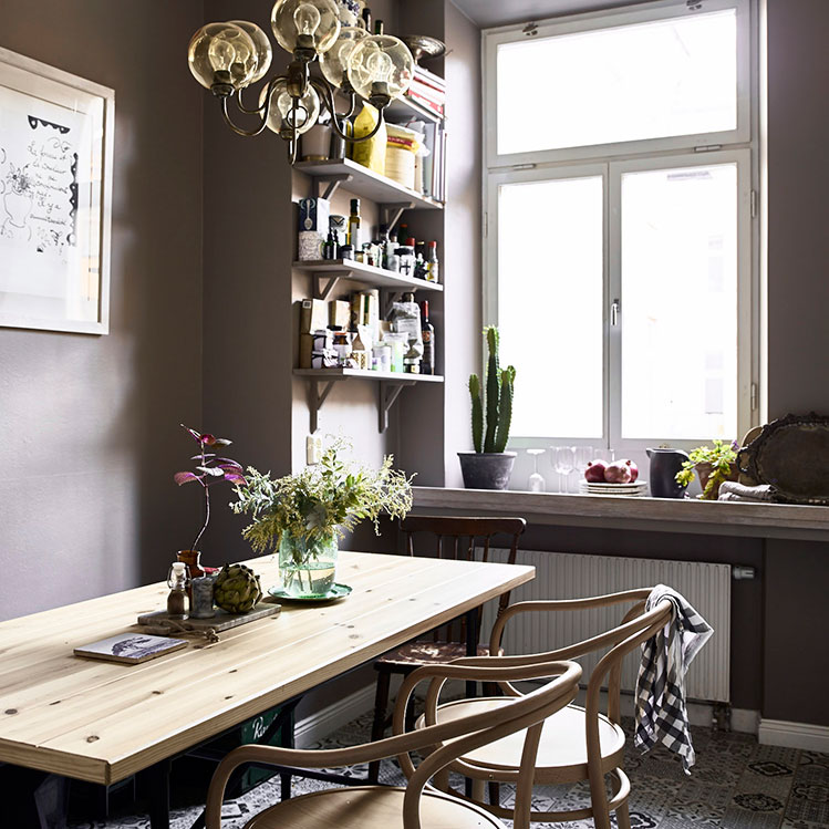 The kitchen is painted grey but mosaic tiles on the floor make it stand out, and natural wood chairs and a dining table add a natural feel