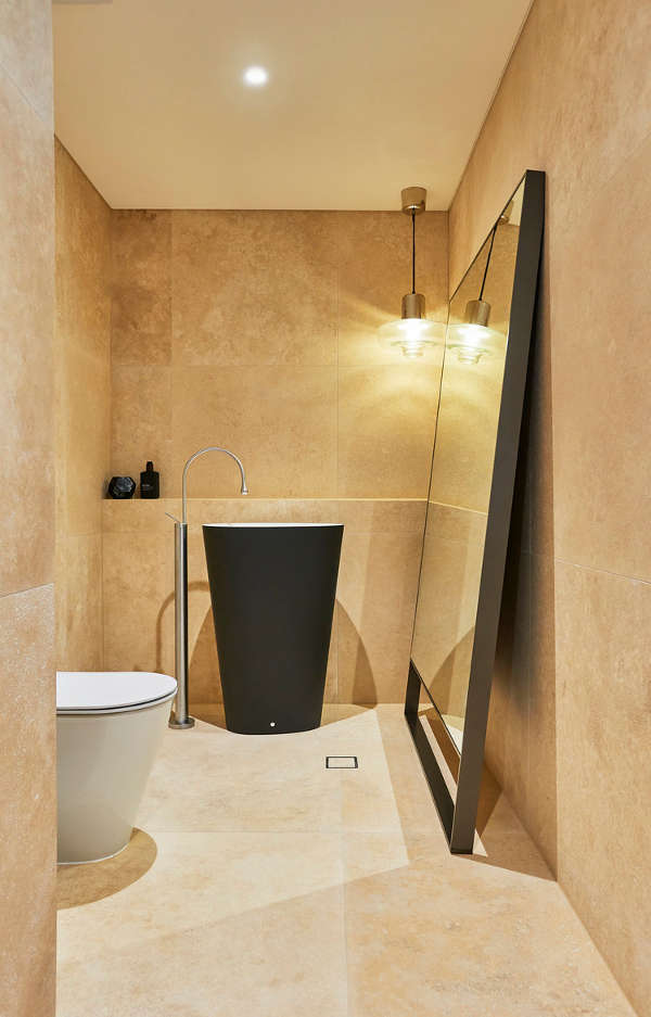 The powder room is done with an oversized floor mirror, a black matte free-standing sink and earthy tiles