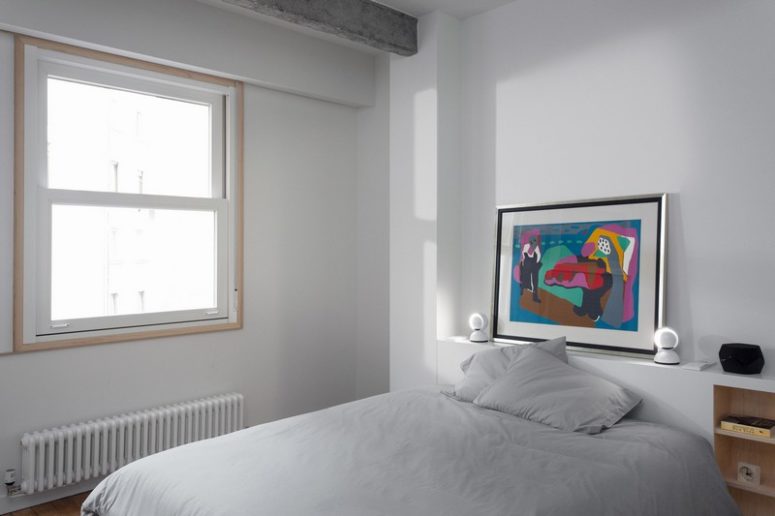 The master bedroom is purely white, there's only a window, a bed, a built-in shelf as a headboard and a bold artwork