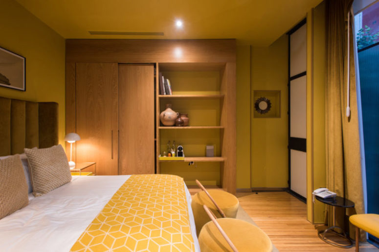 This a yellow guest room with yellow walls, ceiling and textiles, the bed is upholstered with mustard velvet, and there's a large wardrobe