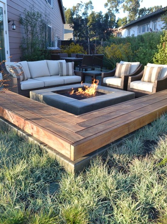 a small and cozy space with upholstered wicker furniture, an L-shaped wooden bench and a fire pit