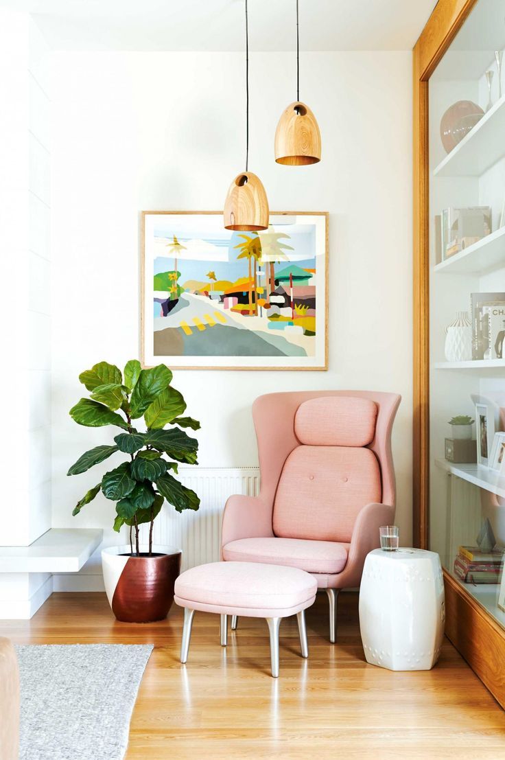 an awkward corner with a pink chair and a footrest, hanging wooden lamps and a side table for reading here