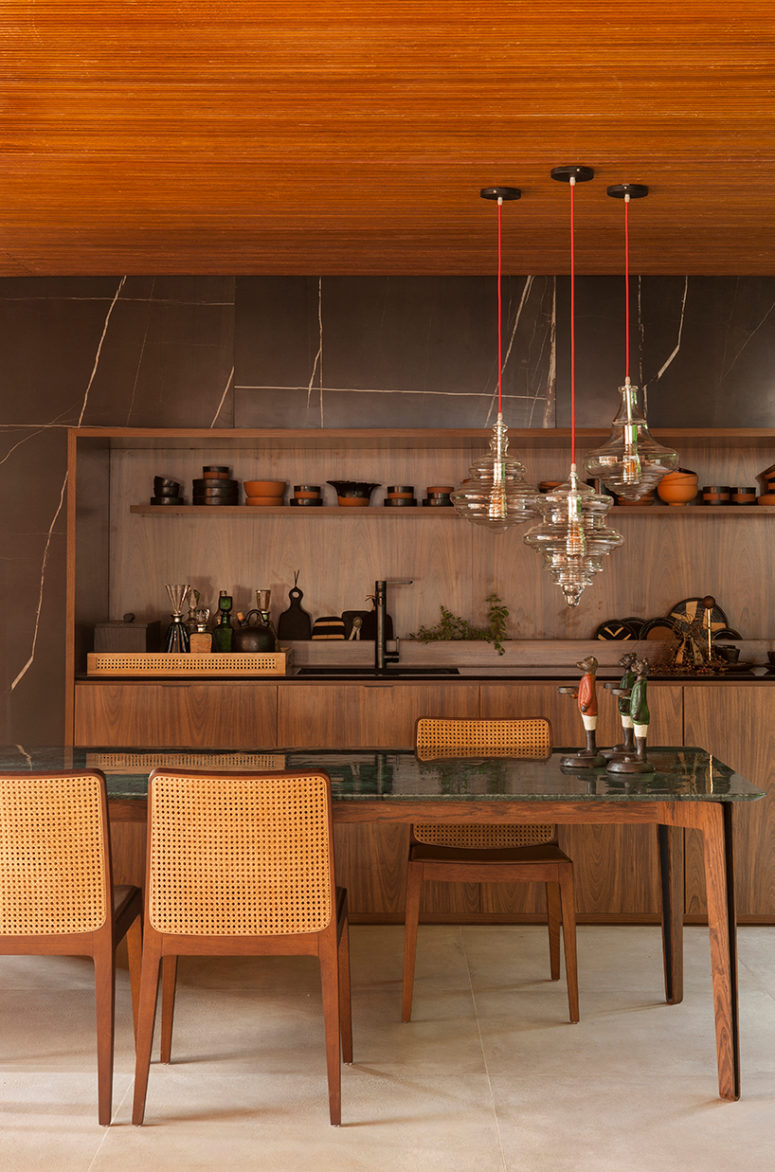 The kitchen is clad with black marble with white veins, and the cabinets are warm-colored wooden ones, a green tabletop finishes the earthy color scheme