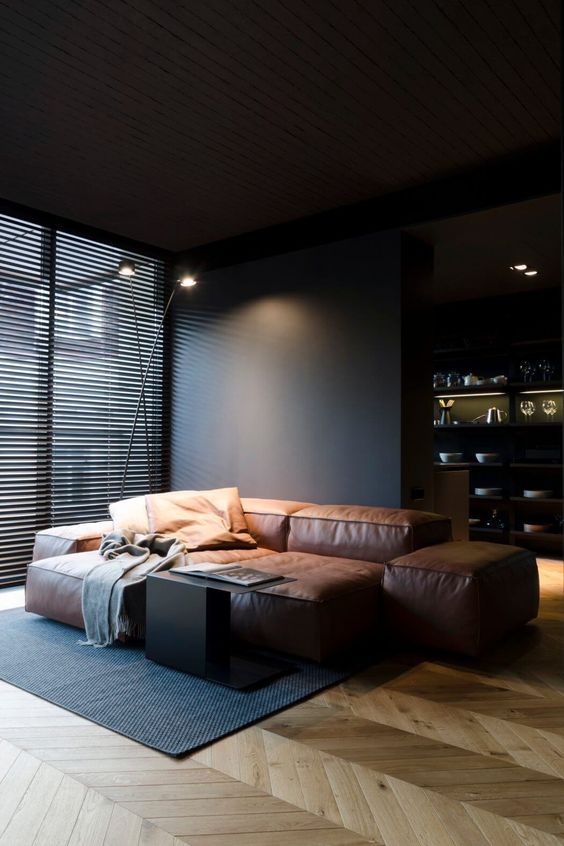a chic masculine space with black walls, a glazed wall, a brown leather sofa and a coffee table is a gorgeous space