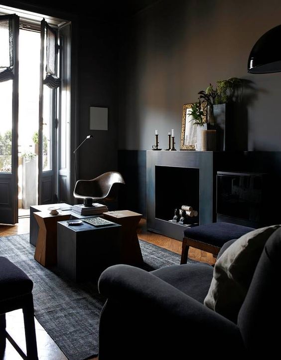 a gorgeous elegant dark space with black walls, furniture, a fireplace and a cluster of coffee tables