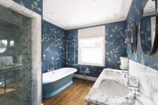 10 The master bathroom is done with navy floral print walls, a marble vanity and shower and a vintage blue bathtub